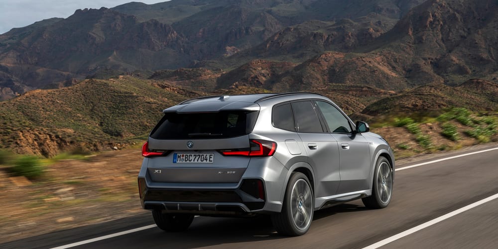 BMW X1 אפור מטאלי בנסיעה, מבט שלושת־רבעי אחורי בהרים